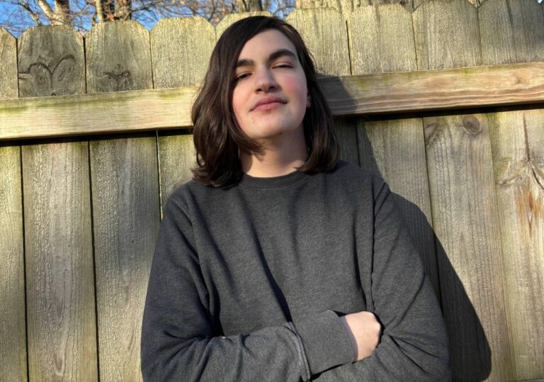 Cameron posing in front of a fence.